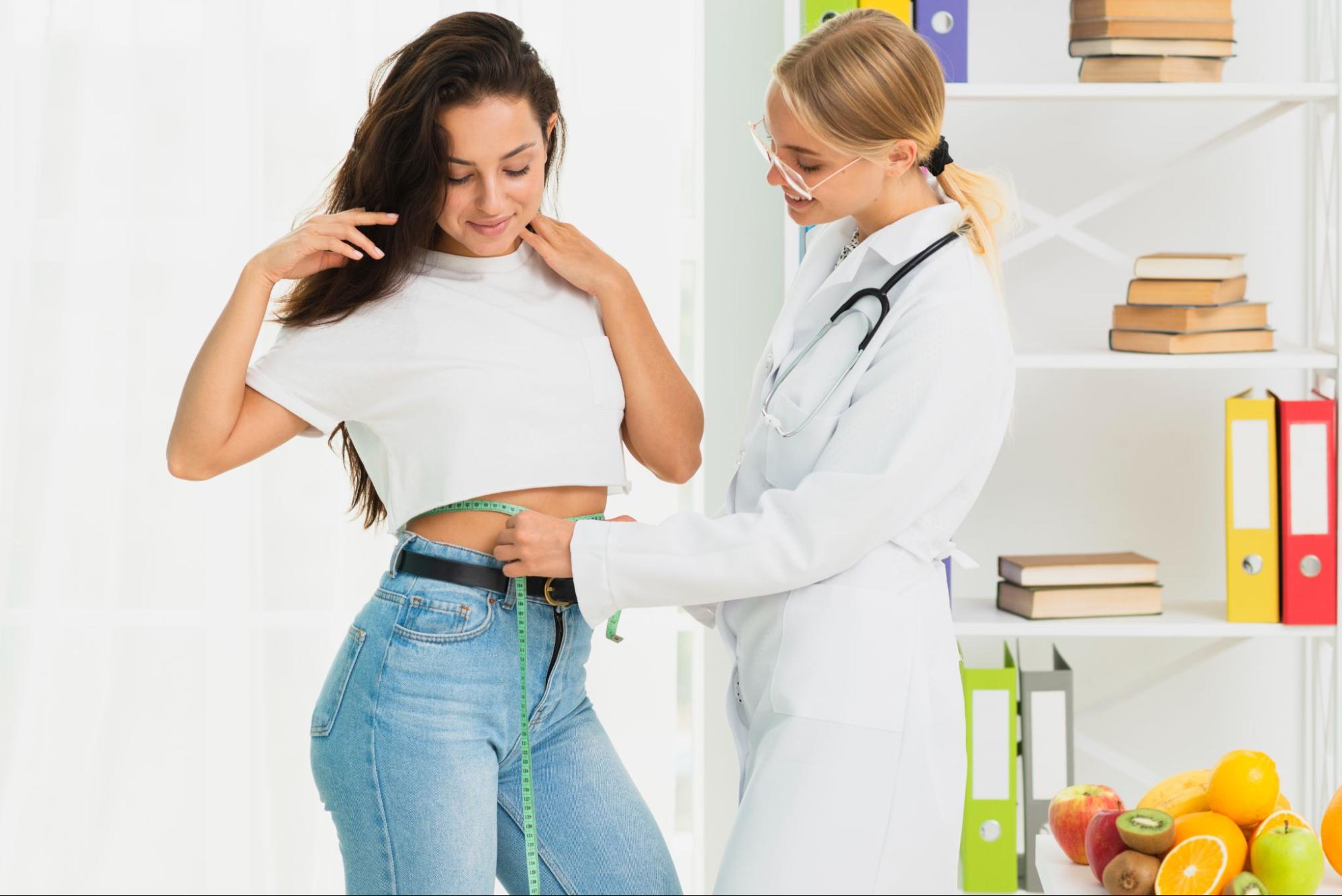 Doctor measuring patient's waist at a medical weight loss clinic with fresh fruits nearby, highlighting a healthy, supervised weight loss approach.